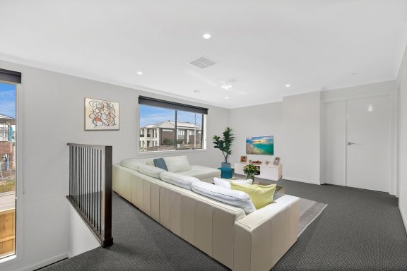 Bright living room with a large sofa, indoor plants, and a TV, featuring modern decor and windows.