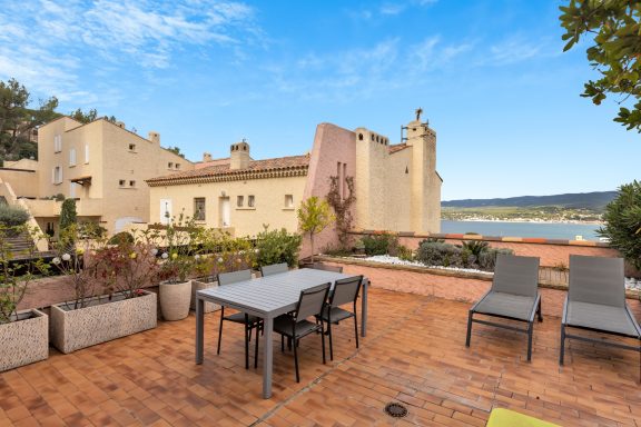 Outdoor patio with a table and chairs overlooking a lake and a historic building.
