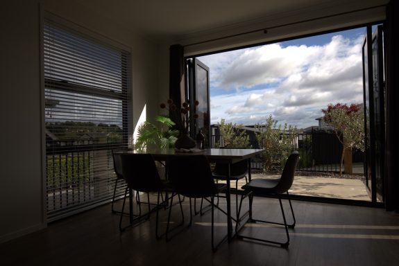 Bright dining area with a table and chairs, open doors leading to an outdoor view.