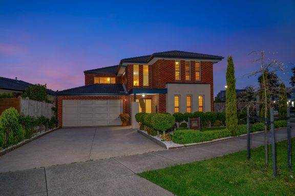 Modern two-story house at dusk with landscaped front yard and glowing windows.