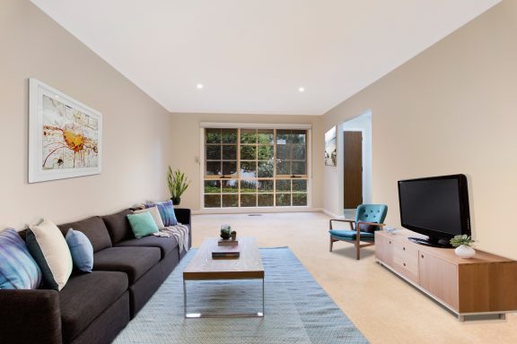 Spacious living room with a sofa, coffee table, TV, and large window letting in natural light.
