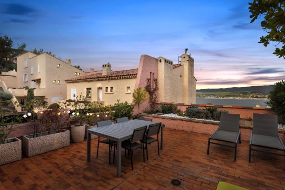 Outdoor patio with a table and chairs, overlooking a scenic landscape at sunset.
