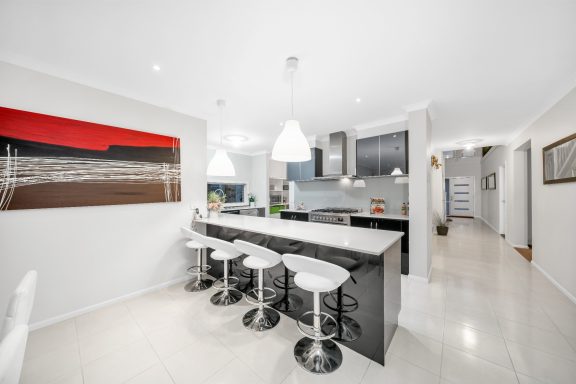 Modern kitchen with a large island, white stools, and contemporary art on the wall.