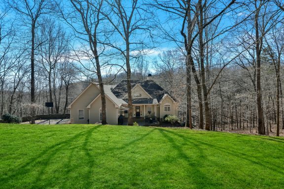 A cozy house surrounded by trees and green grass under a blue sky.