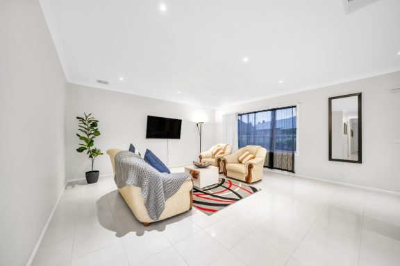 Bright living room with two chairs, a sofa, a TV, and large windows showcasing outdoor views.